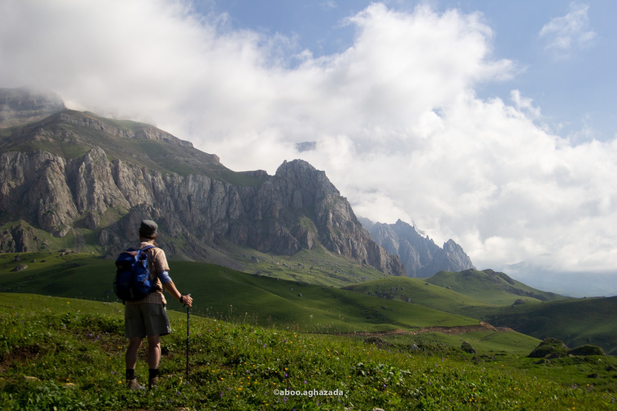 Hiker looking out at cloud-wrapped jagged mountain peaks from a wildflower meadow, Azerbaijan