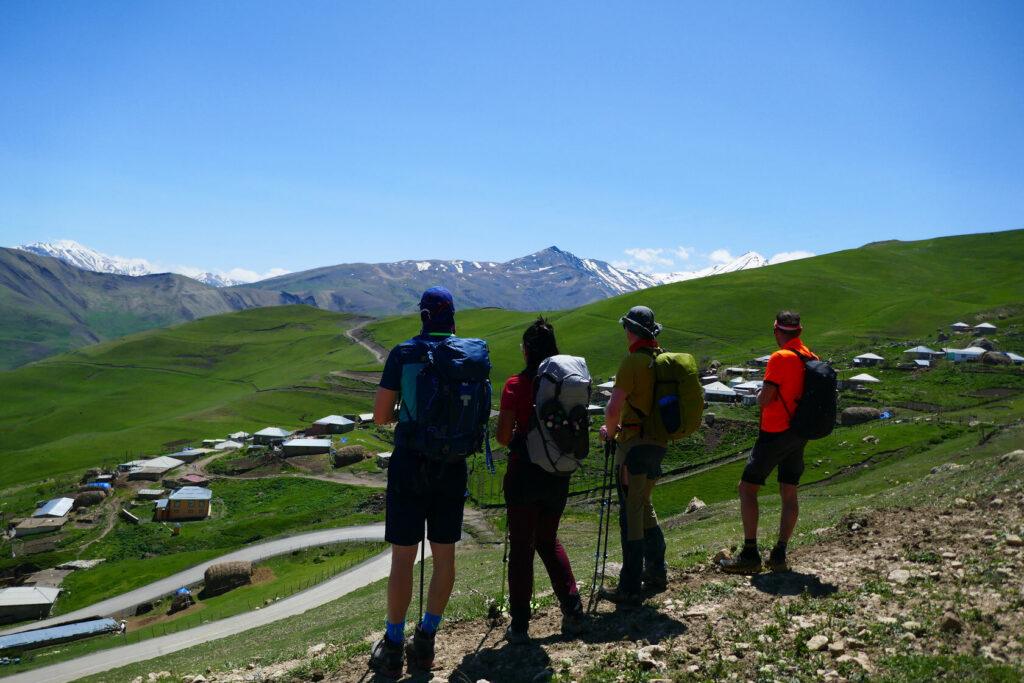 Group of hikers looking out over green hills toward snow-capped Caucasus peaks, Azerbaijan
