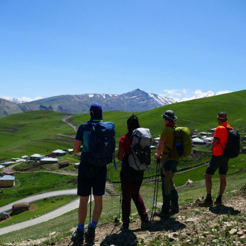 Group of hikers looking out over green hills toward snow-capped Caucasus peaks, Azerbaijan