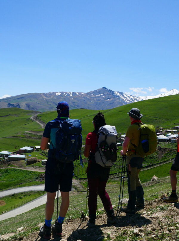 Group of hikers looking out over green hills toward snow-capped Caucasus peaks, Azerbaijan