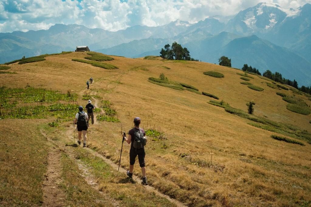 Hikers descending a golden grassy hillside trail in Svaneti, Georgia