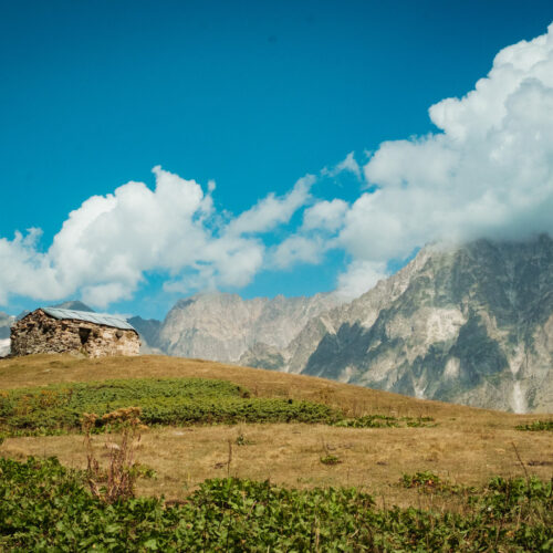 Stone Svan tower on a ridge with a rocky peak behind, Svaneti, Georgia