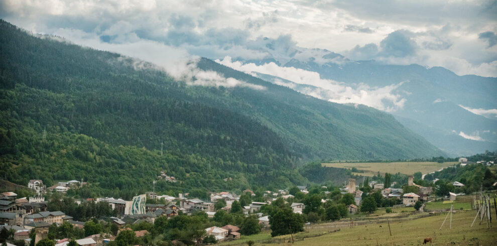Svan tower village in a green valley beneath cloud-wrapped peaks, Svaneti, Georgia