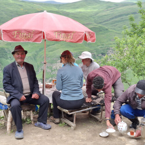 Hikers and local villagers gathered under a red canopy at a village stop in Azerbaijan
