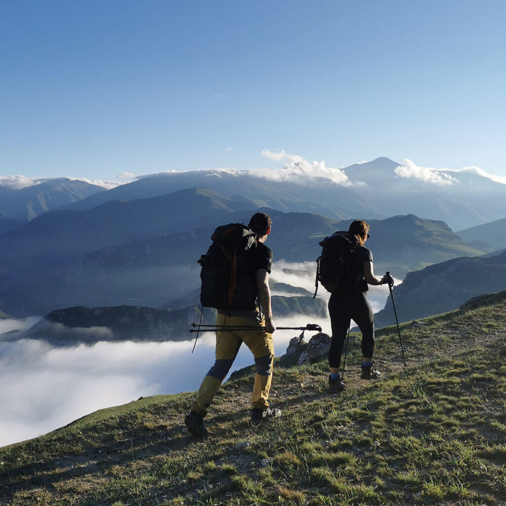 Two hikers walking a ridge above a sea of clouds filling the valley below, Azerbaijan